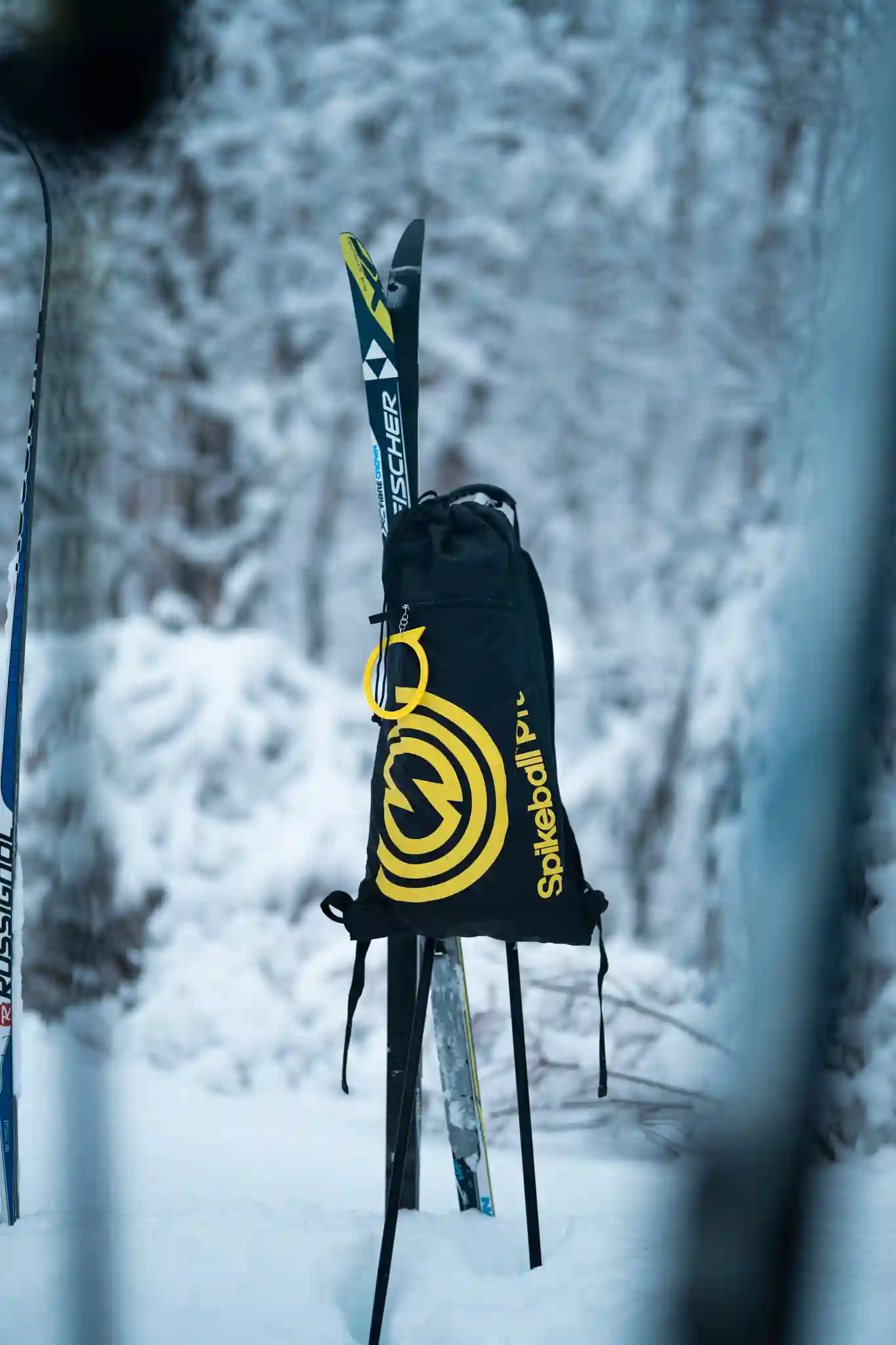Schwarzer Spikeball Pro Rucksack mit gelbem Logo steht zwischen Skiern im Schnee – Outdoor‑Tasche im Winter