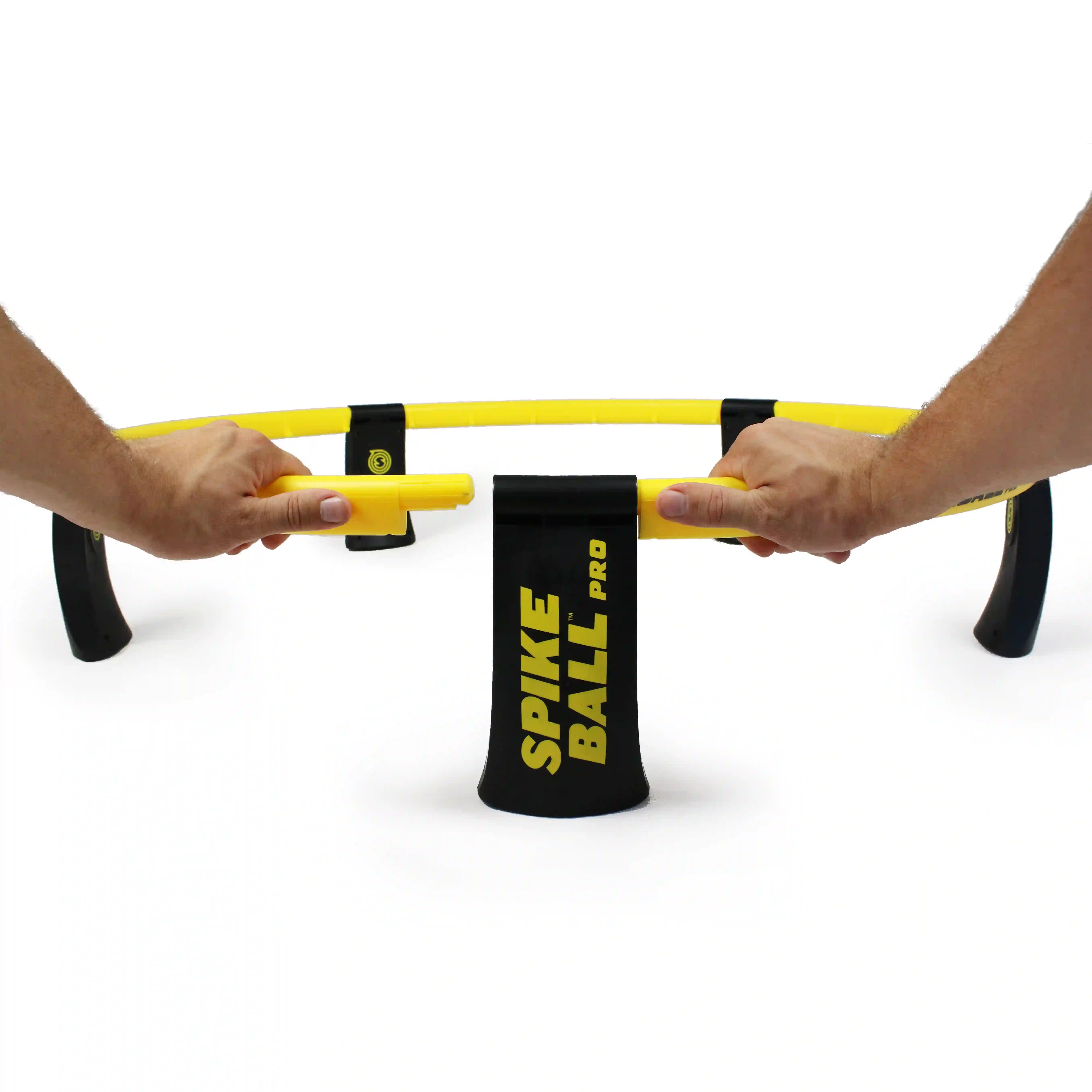 Hände verbinden gelbe Rahmenteile des Spikeball‑Pro‑Sets, schwarze Beine mit gelber Aufschrift sichtbar