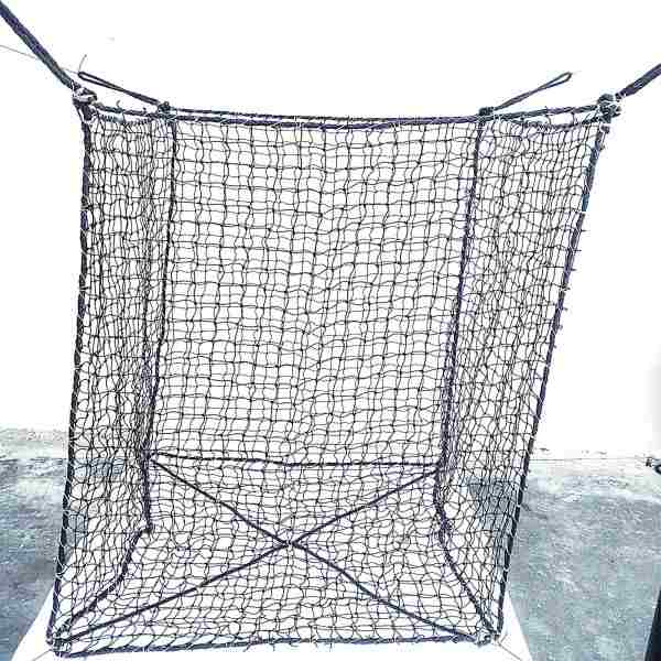 Großer würfelförmiger Netzkorb Woodbag aus schwarzen Schnüren steht auf einem Betonboden vor einer weißen Wand. Die Unterseite ist mit überkreuzten Verstärkungsseilen gesichert