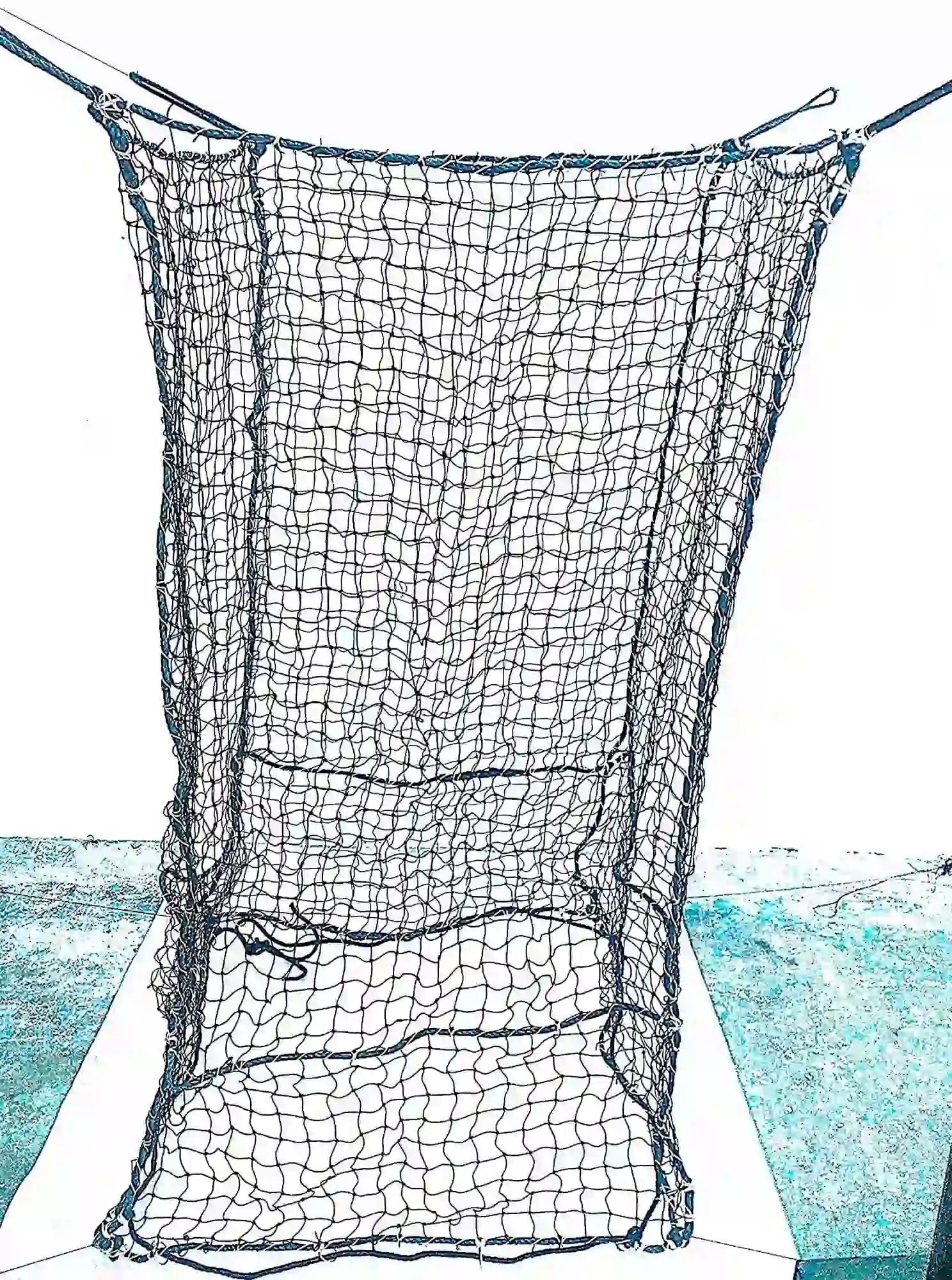 Großer würfelförmiger Netzkorb Woodbag aus schwarzen Schnüren steht auf einem Betonboden vor einer weißen Wand. Die Unterseite ist mit überkreuzten Verstärkungsseilen gesichert