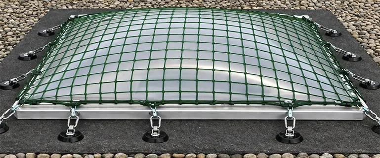 Domförmige Lichtkuppel auf Flachdach mit grünem, knotenlosem Sicherheitsnetz aus hochfestem Polypropylen (5 mm Fadenstärke, 100 mm Maschenweite) zur Absturzsicherung, befestigt mit Karabiener und Ketten