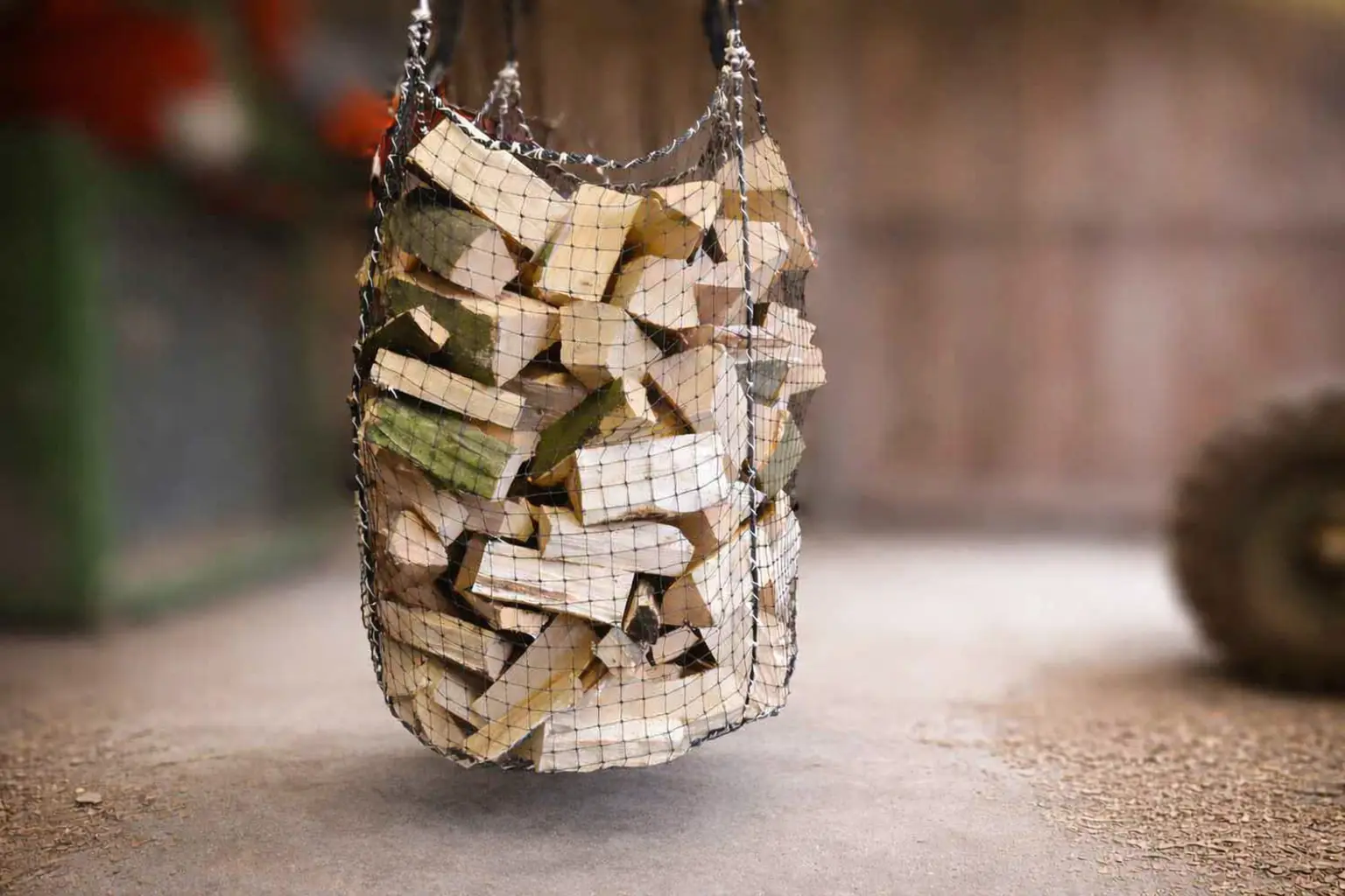 Netzsack mit gespaltenem Brennholz hängt über dem Sandboden in einer Werkstatt; Holzlagerung und Feuerholztransport im Fokus