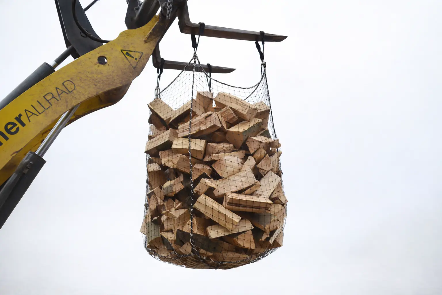 Radlader transportiert Netzsack mit gespaltenem Brennholz in der Luft – effiziente Lösung für Feuerholztransport und Holzlagerung.