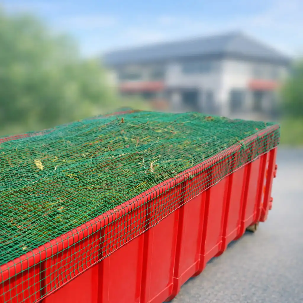 Roter Container mit Gartenabfall, der mit einem grünen Abdecknetz gesichert ist.